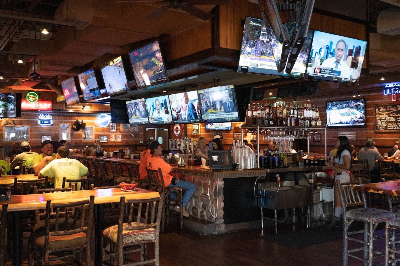 A sports lounge with screens above a long bar and seating.