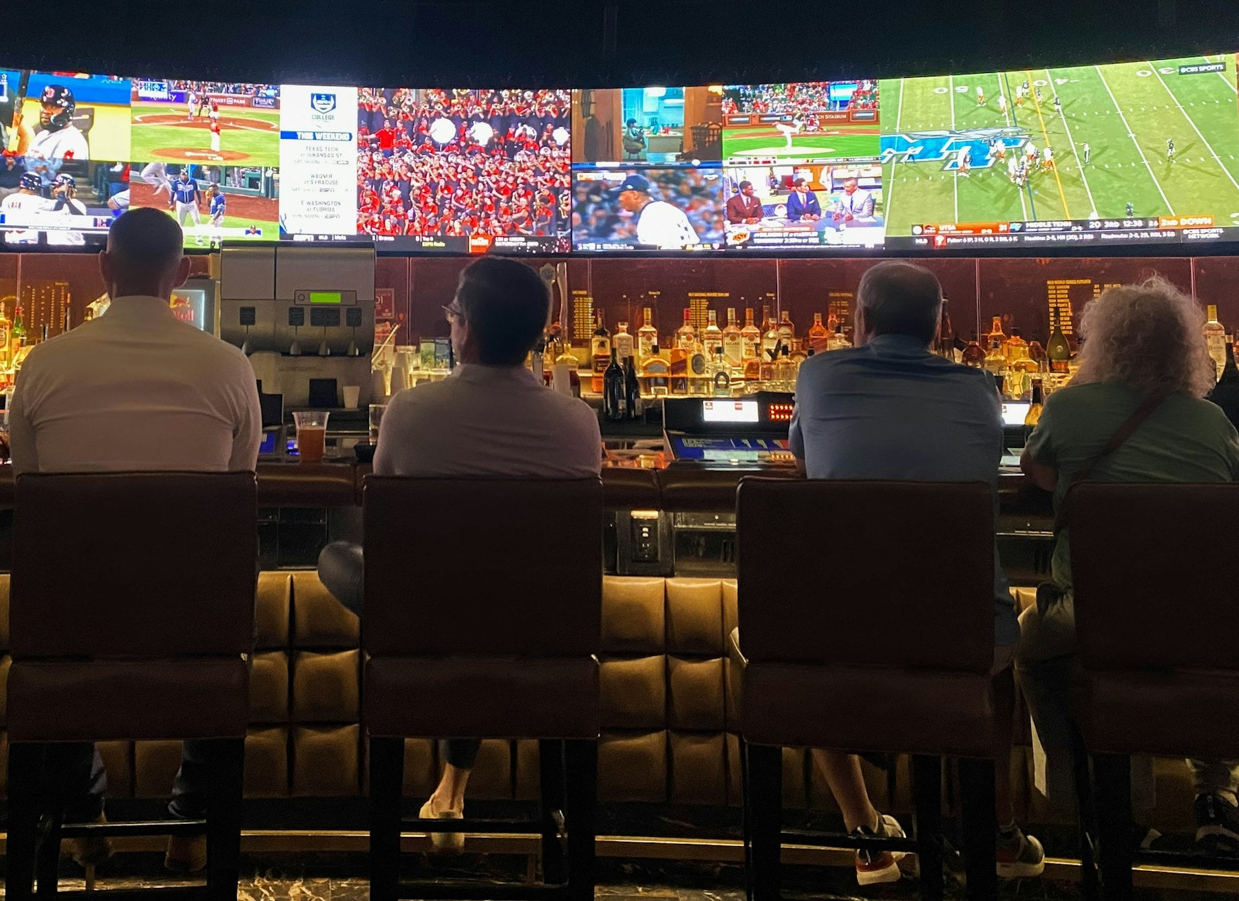 People seated at a bar in front of a wall of screens showing live sport.
