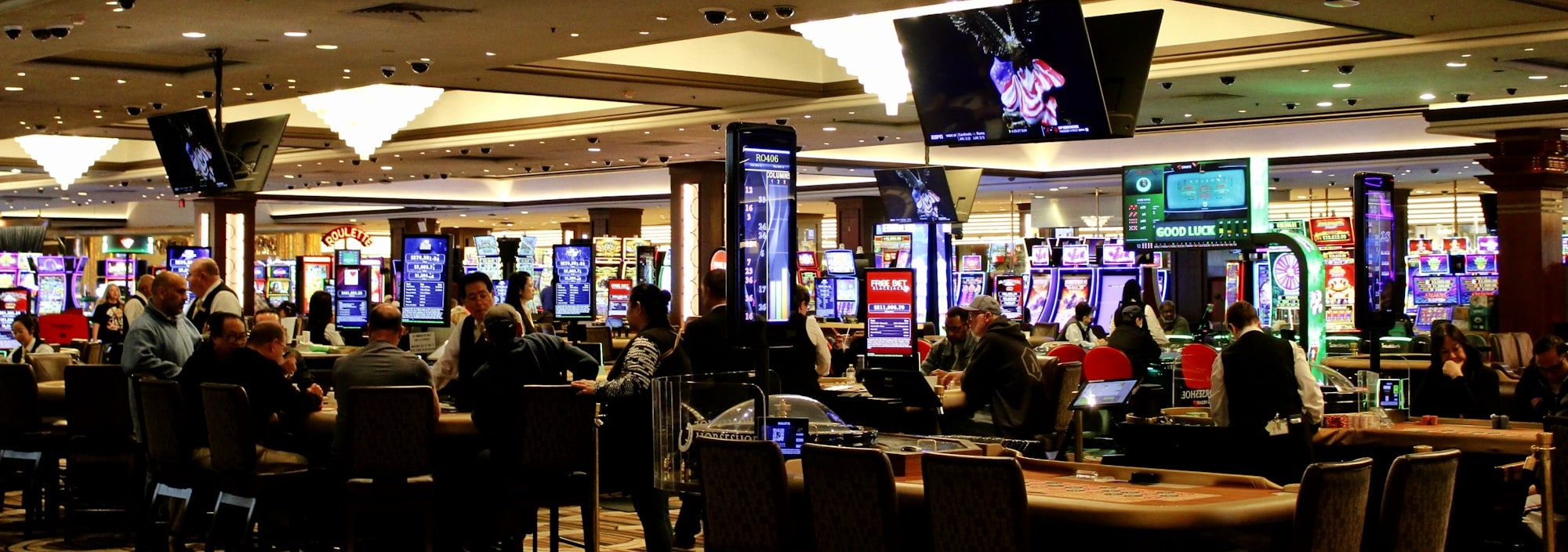 A busy casino floor of gaming tables and machines with dealers and guests.