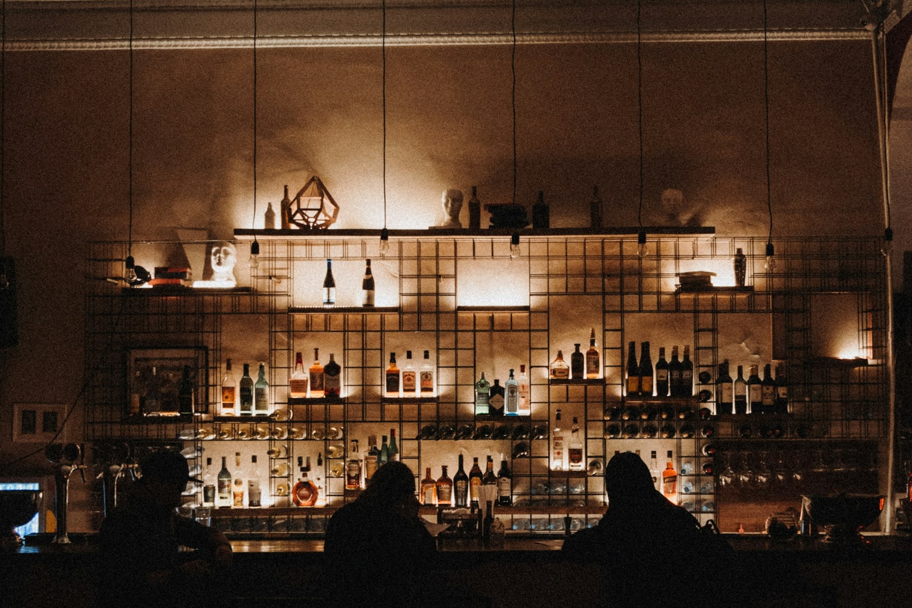 Two people seated at a dimly lit bar with backlit bottles behind them.