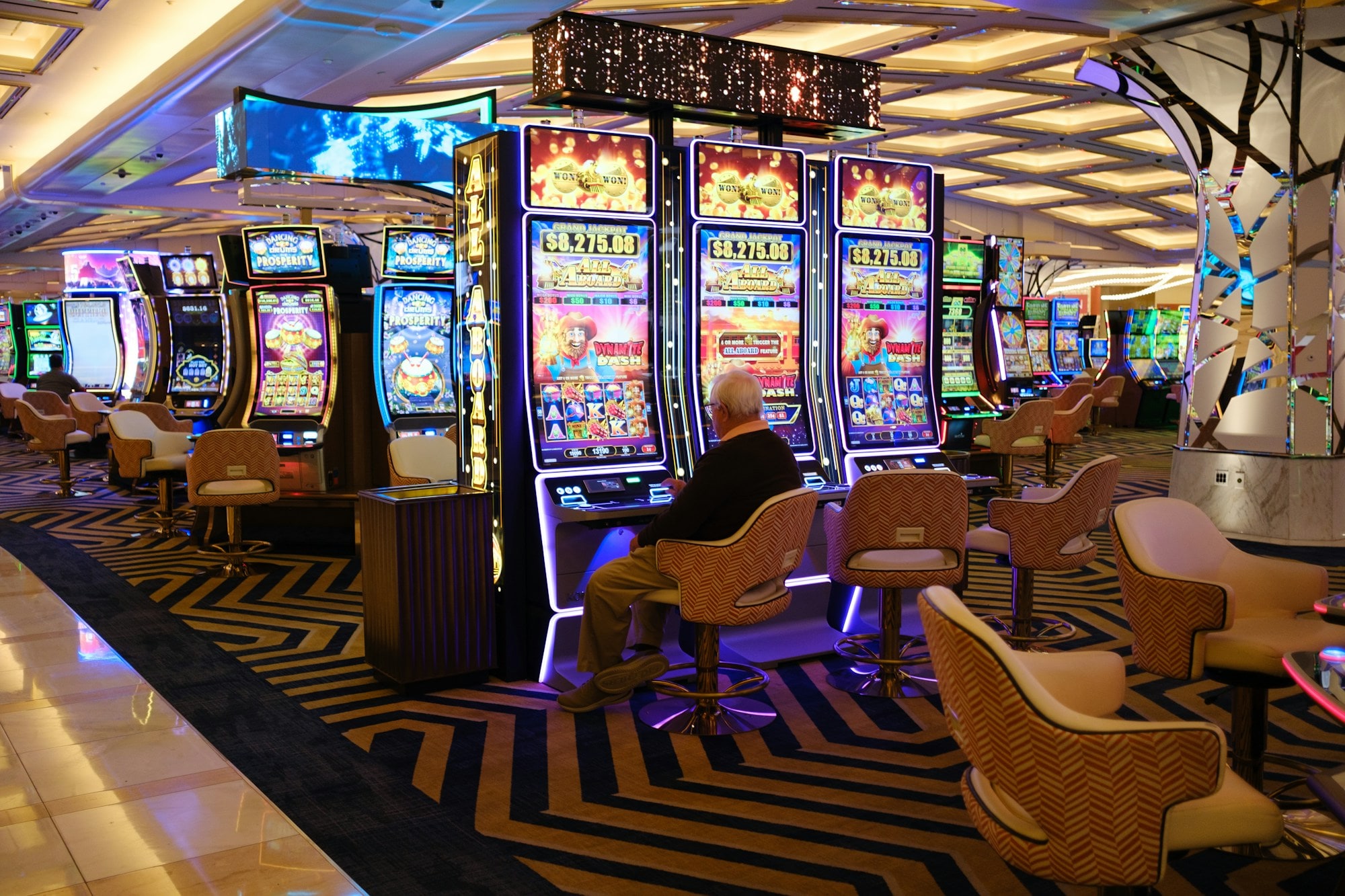 A calm, modern gaming-machine lounge with leather stools and a marble floor.
